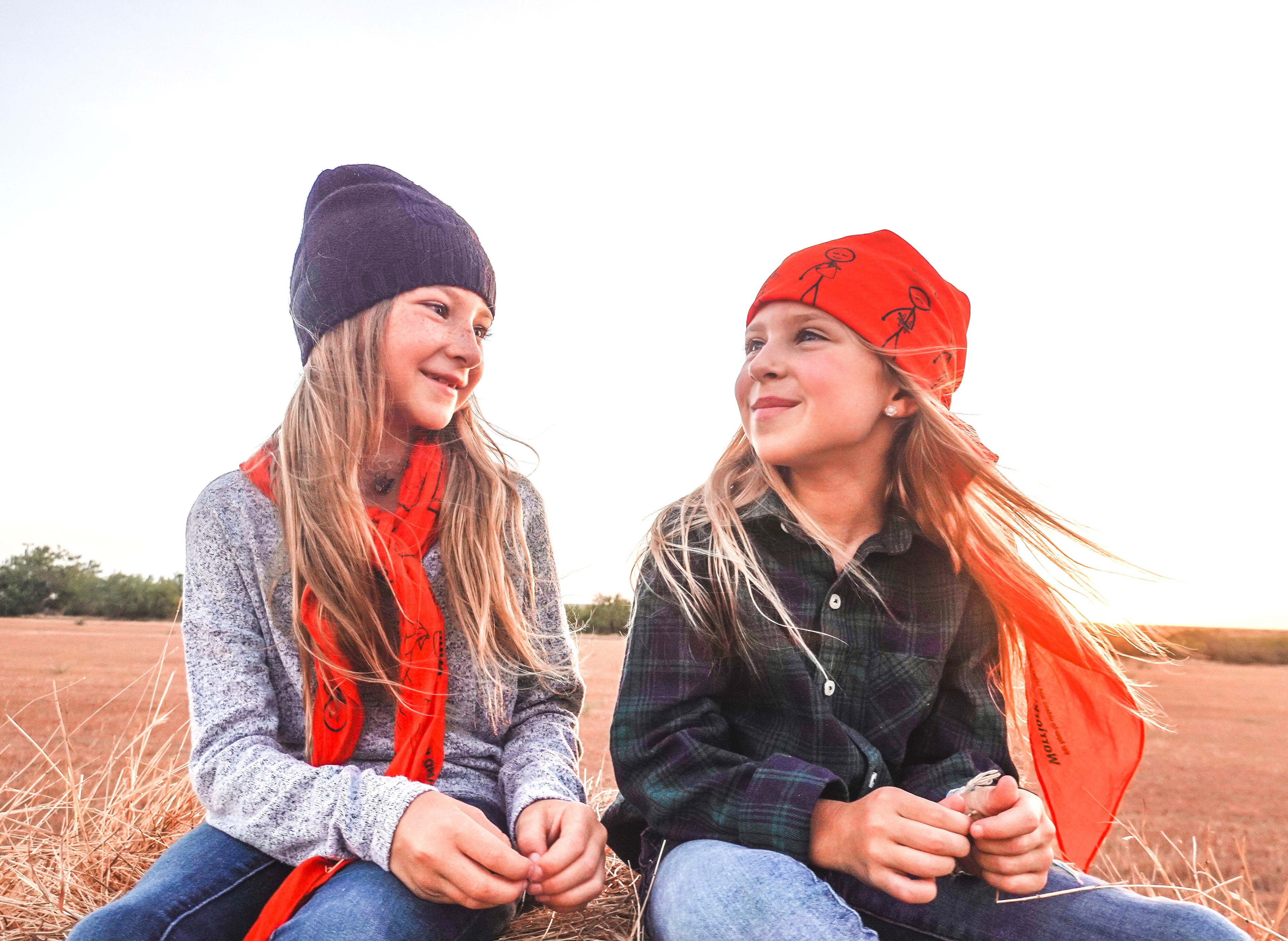 2 people wearing the triangular bandage multi tool. one wearing it as a scarf and on wearing it wrapped on their head