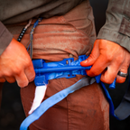 someone applying a blue CAT tourniquet to their leg